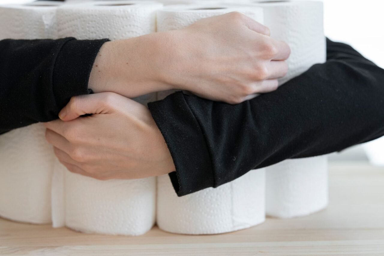 Arms holding a stack of toilet paper rolls, symbolizing comfort and cleanliness.