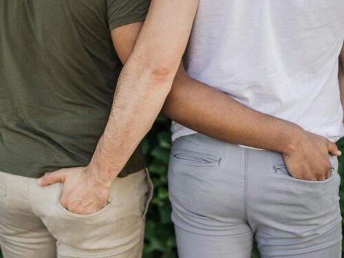 Interracial gay couple holding hands, symbolizing love and togetherness. Back view outdoors on a sunny day.