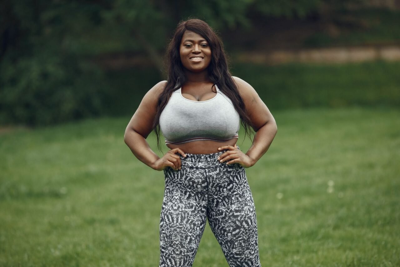 Smiling African American woman in activewear posing in a grassy field.