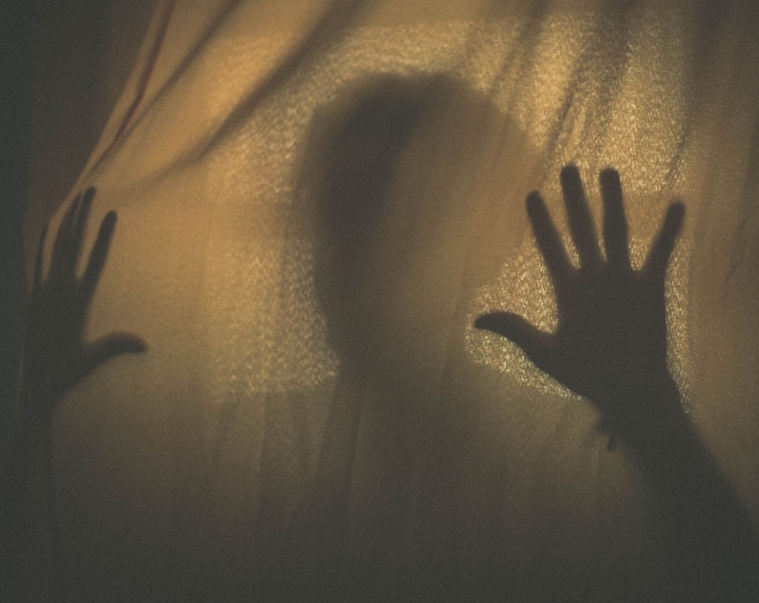 Silhouette of a person with hands pressed against a fabric curtain, creating a mysterious shadow.