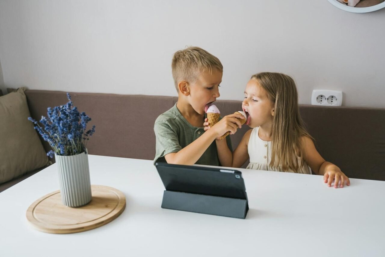 Two kids happily sharing an ice cream cone in a cozy indoor setting.