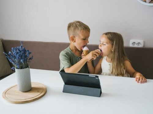 Two kids happily sharing an ice cream cone in a cozy indoor setting.