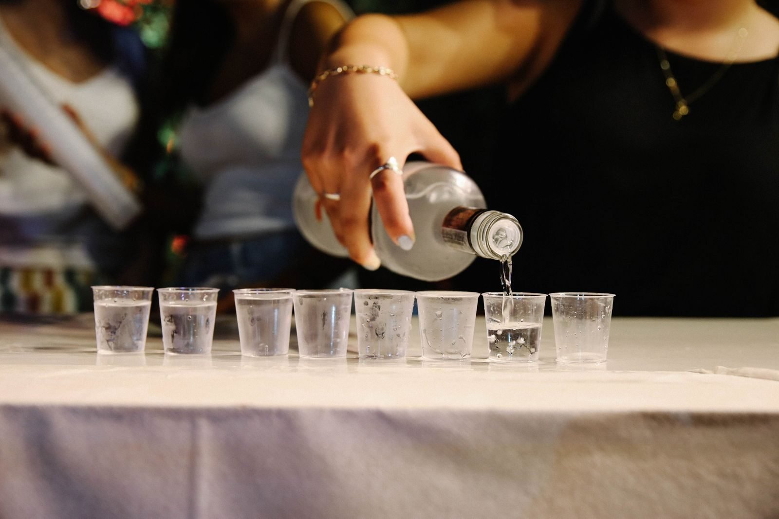 Close-up of a woman pouring vodka into shot glasses on a table, capturing a lively party atmosphere.