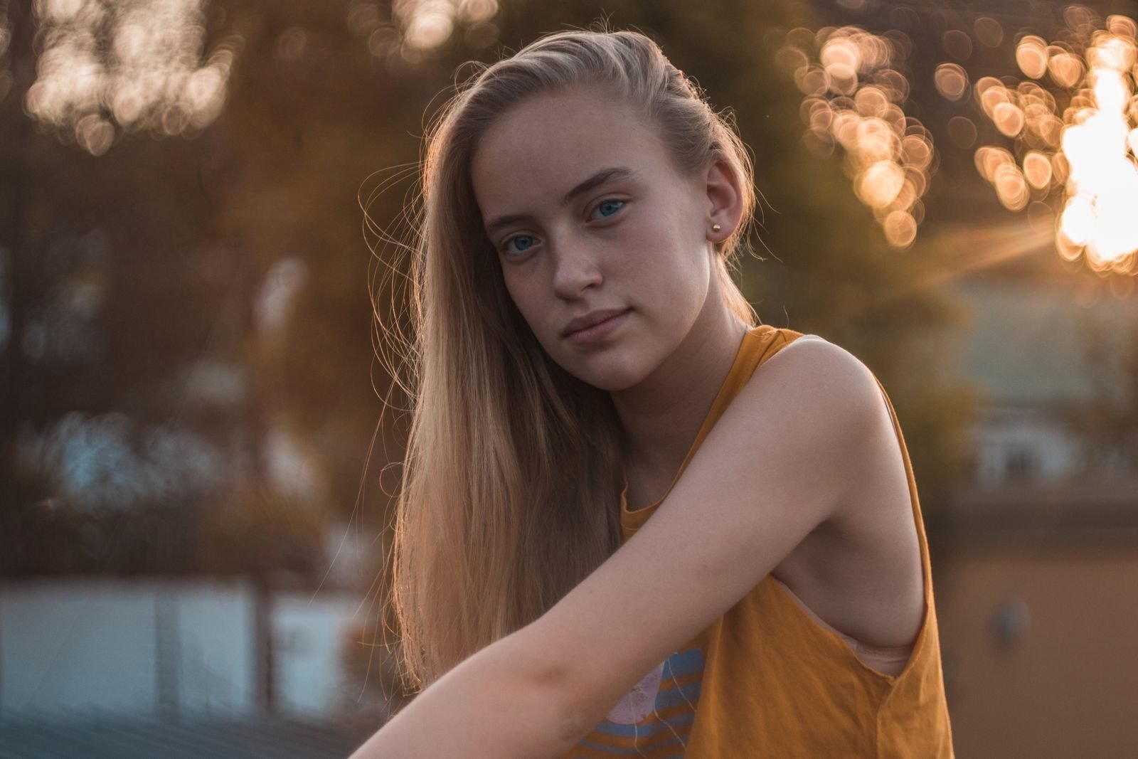 Captivating outdoor portrait of a young woman in a yellow tank top during golden hour.