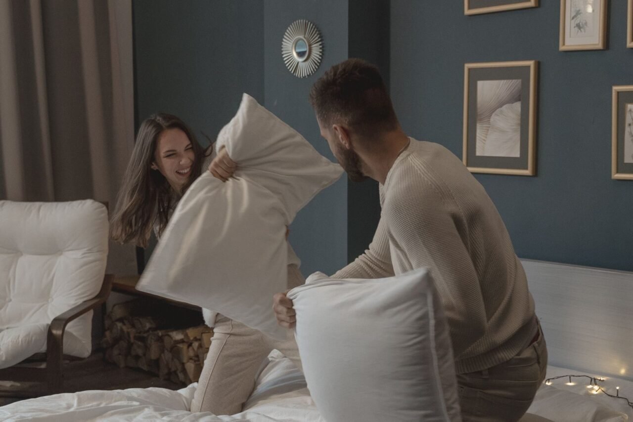 A happy couple enjoying a playful pillow fight indoors, capturing a moment of joy and togetherness.