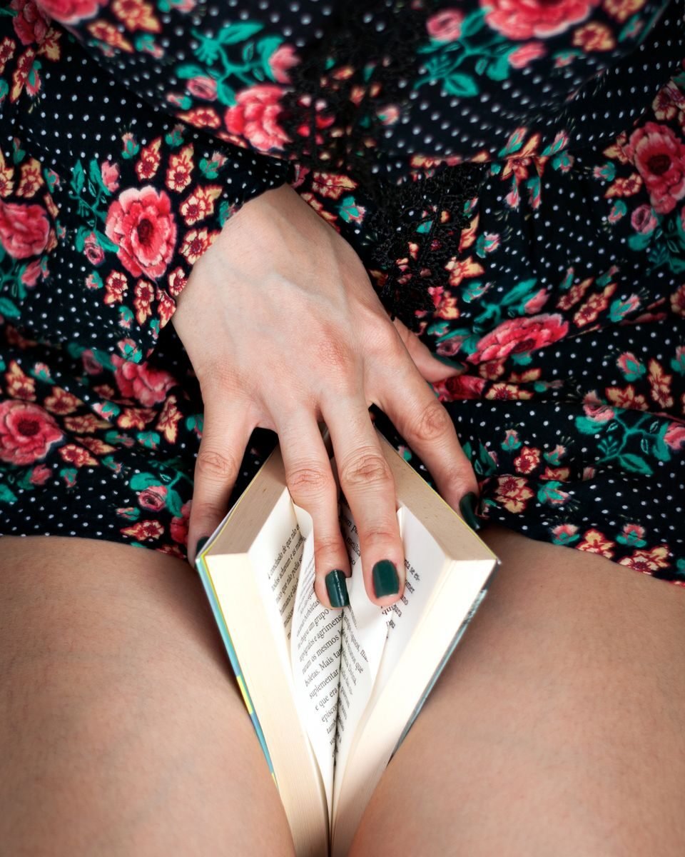 Close-up of a woman's hand holding a book on her lap, wearing a floral dress.