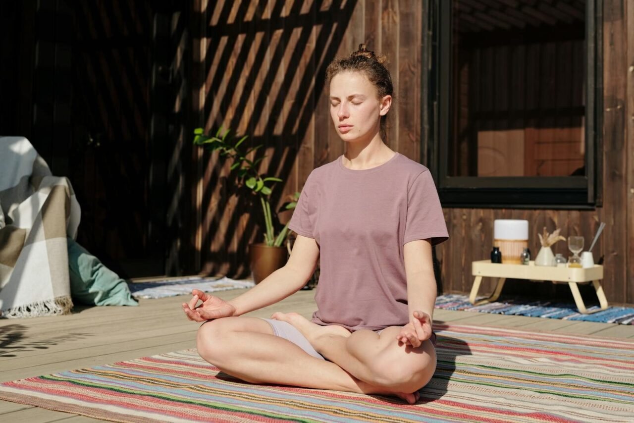 Woman practicing meditation in lotus pose on a sunny outdoor deck.