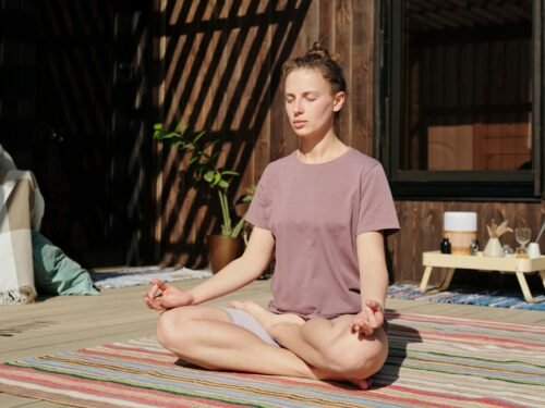 Woman practicing meditation in lotus pose on a sunny outdoor deck.