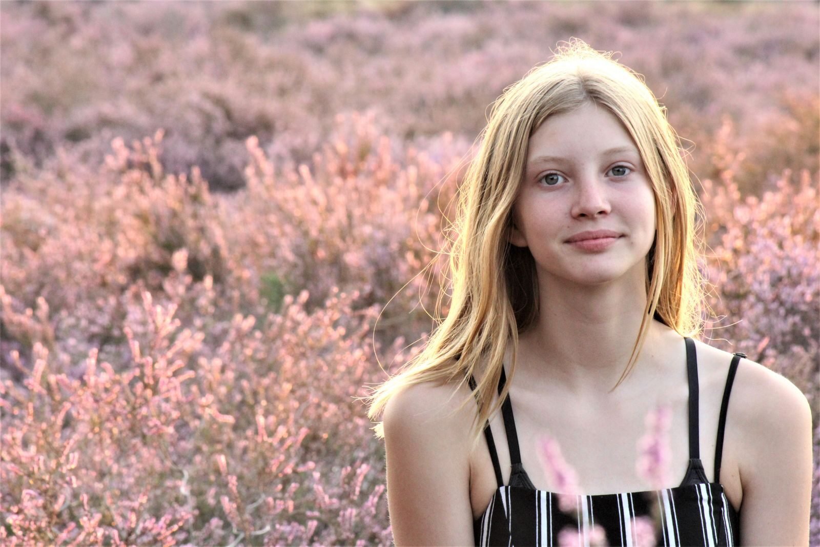 A young woman in a spaghetti strap dress poses in a pink flower field.