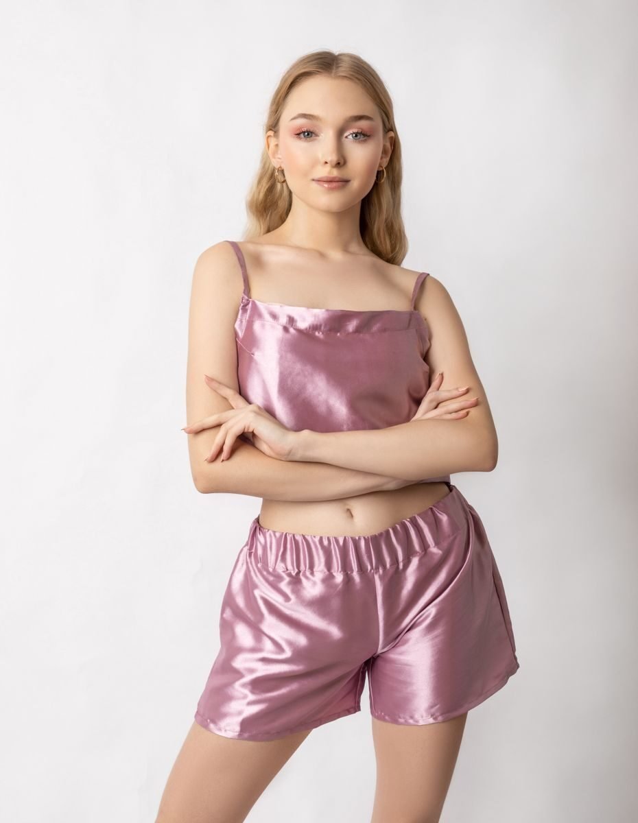 Serious young female model with hands crossed wearing pink silk pajama made of shorts and top