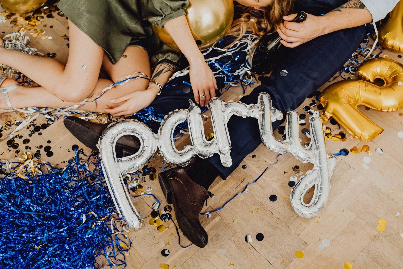A lively indoor party scene with balloons, confetti, and people lying on the floor.