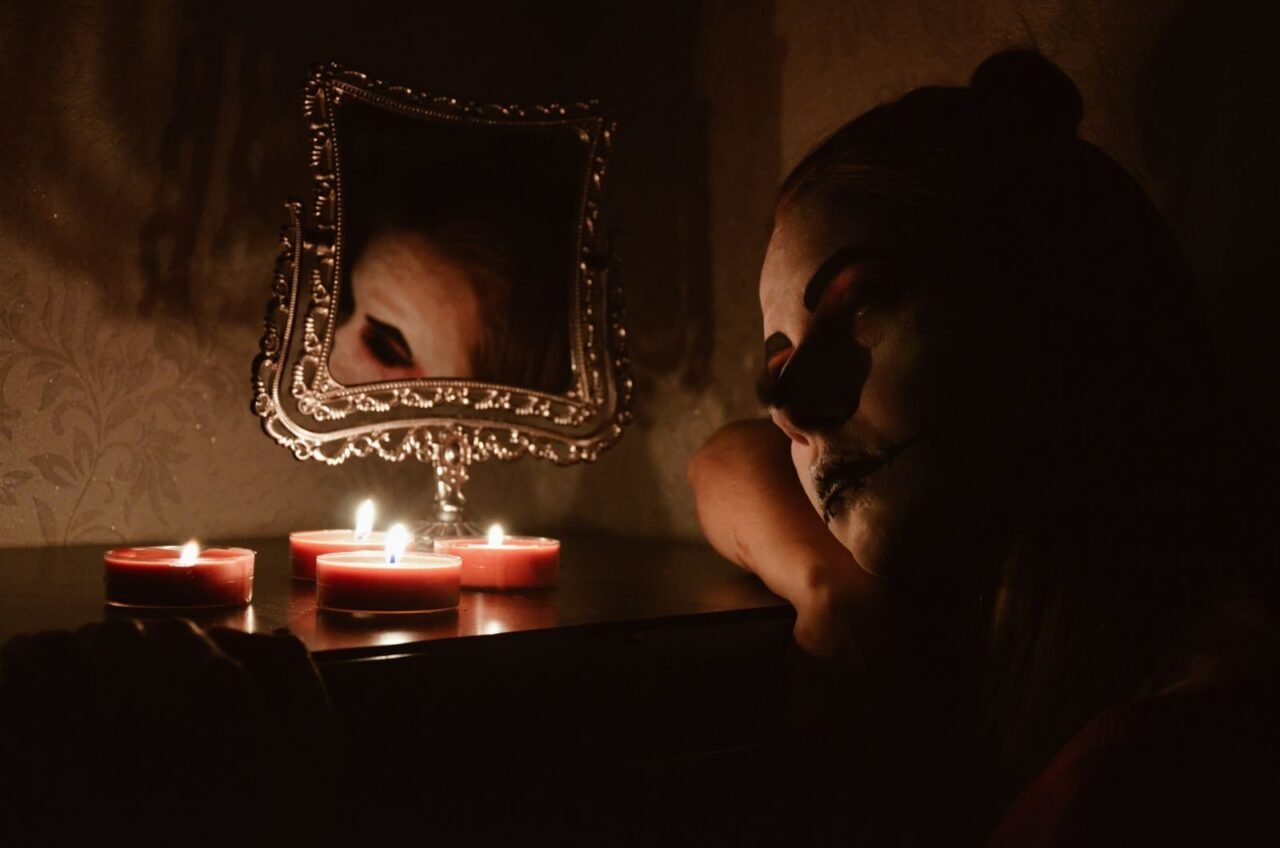 Spooky Halloween scene with a woman in makeup and candles, reflecting in an ornate mirror.