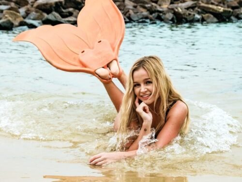 woman lying on seashore wearing orange flippers near stones during daytime