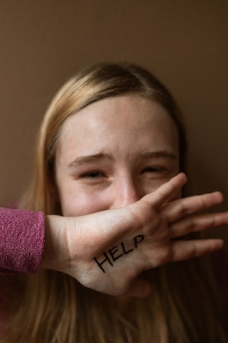 A distressed teenager covering face with 'HELP' written on hand, signifying need for support.