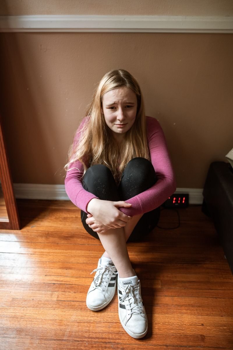 Teenage girl sitting on a wooden floor appearing distressed indoors.
