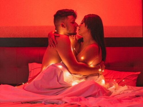 Passionate couple embracing under a warm red glow, wrapped in string lights for a cozy intimate atmosphere.