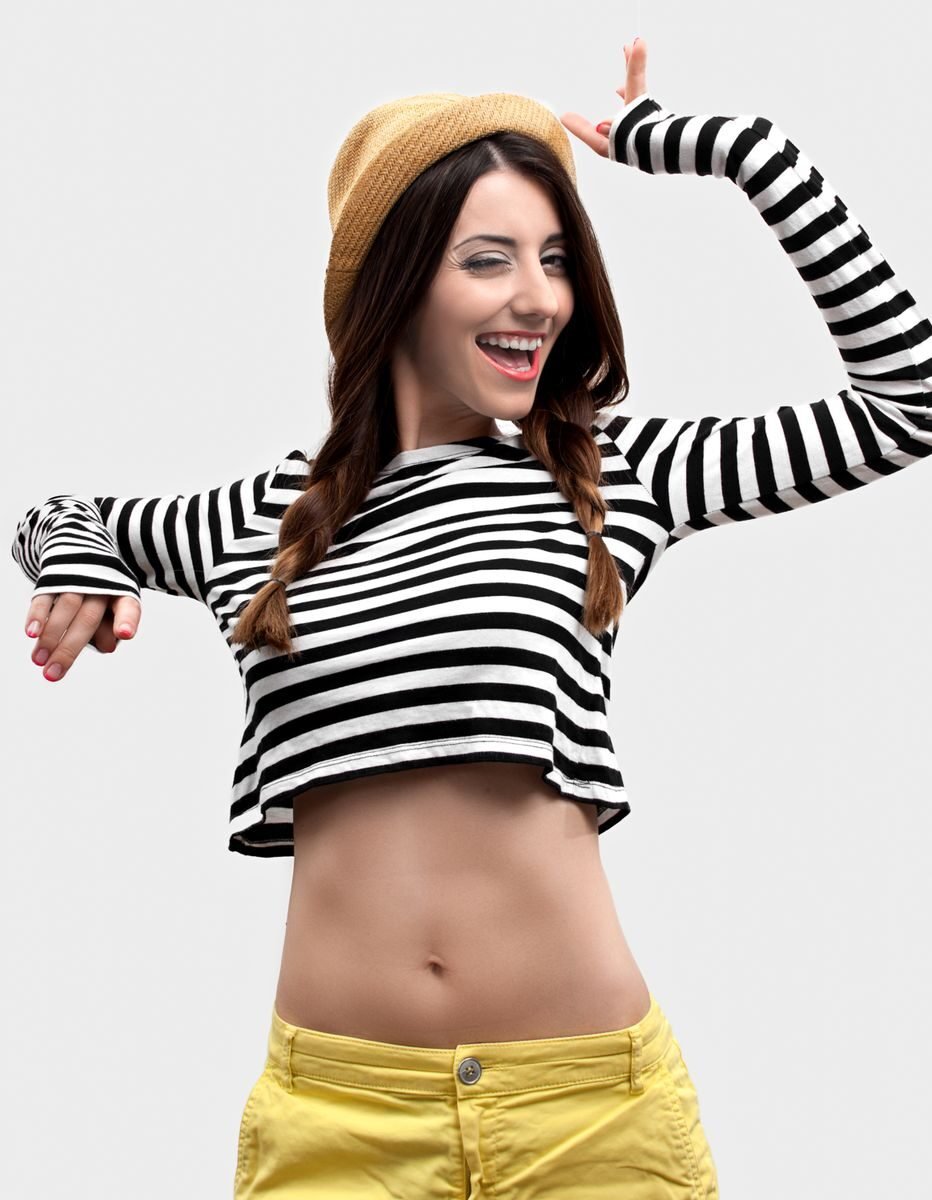 Cheerful young woman in a striped crop top and straw hat posing playfully with a bright smile.