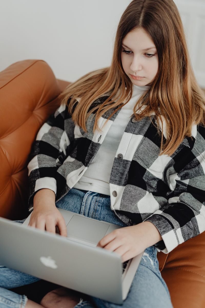 Teenage girl sitting on sofa with a laptop, engaged in online learning.
