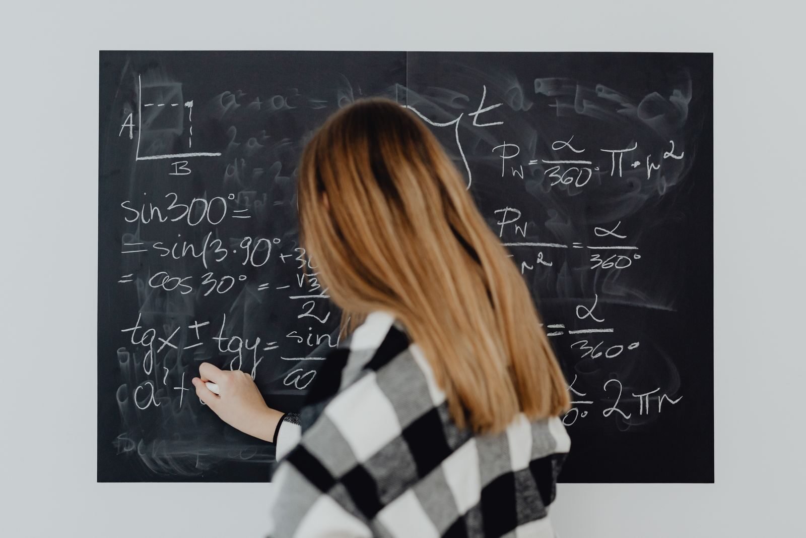 A woman writing mathematical equations on a blackboard, illustrating education and learning.