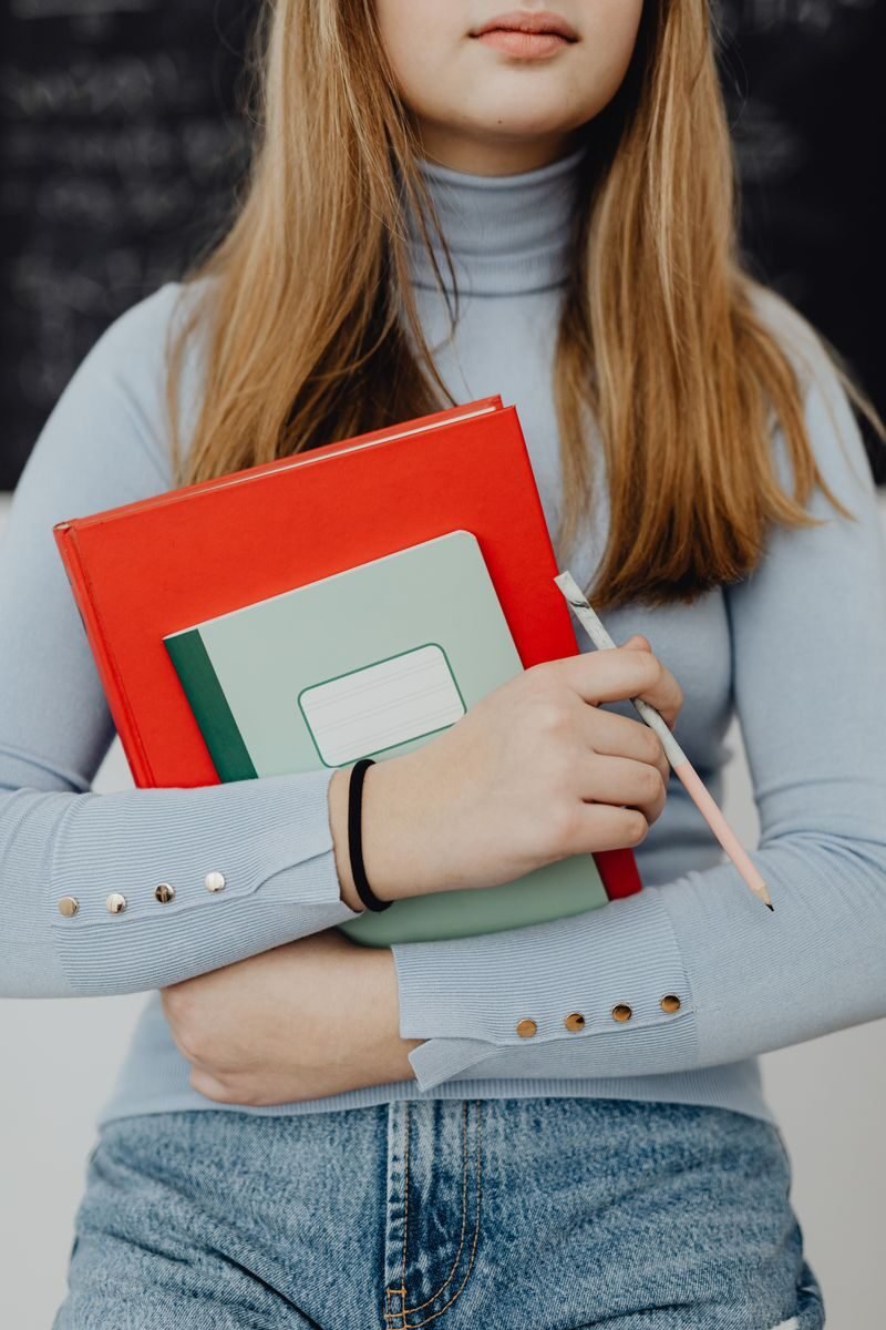 Teenage girl holding textbooks and a pen in a classroom setting, embodying education.