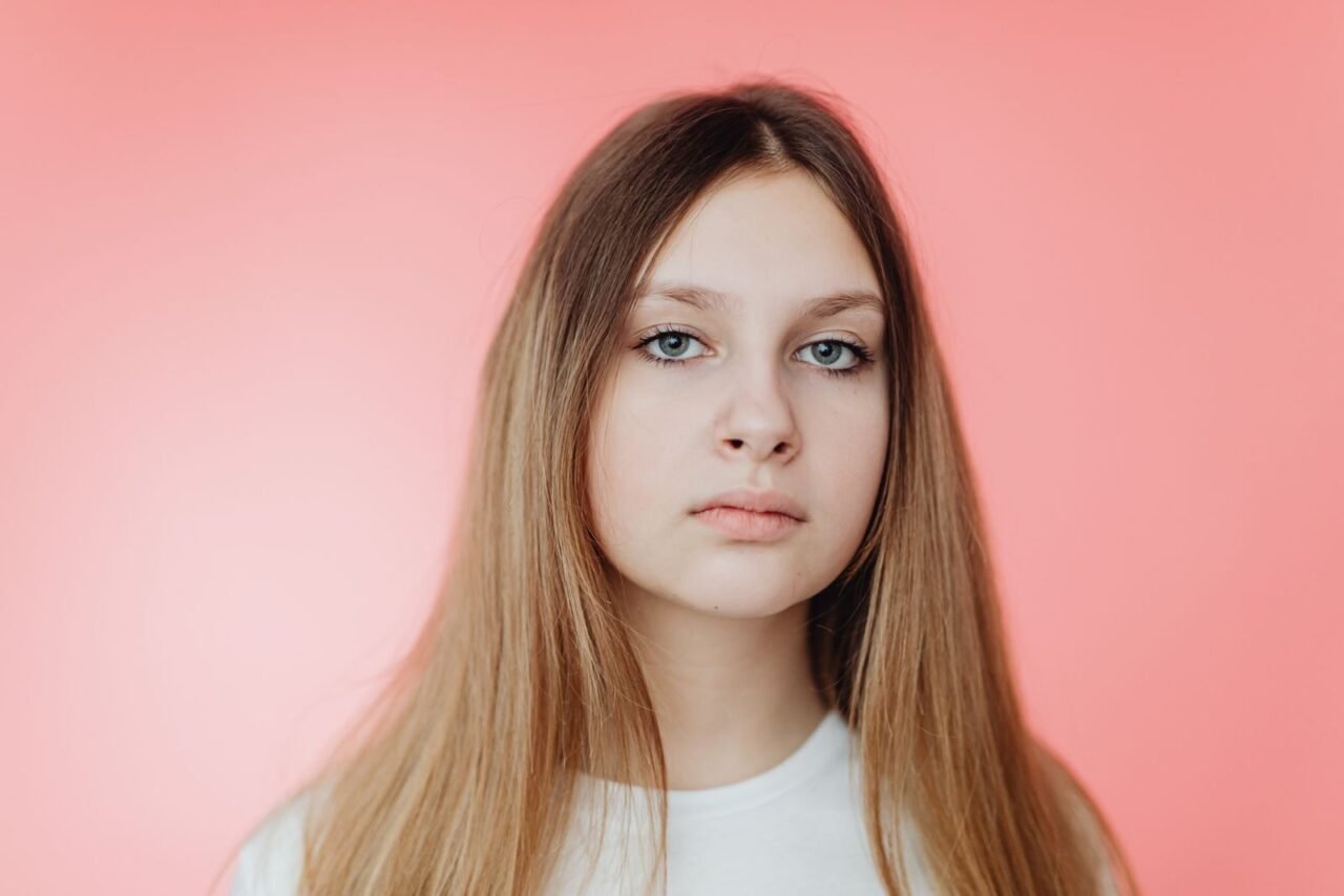 Studio portrait of a young woman with long hair on a pink background.