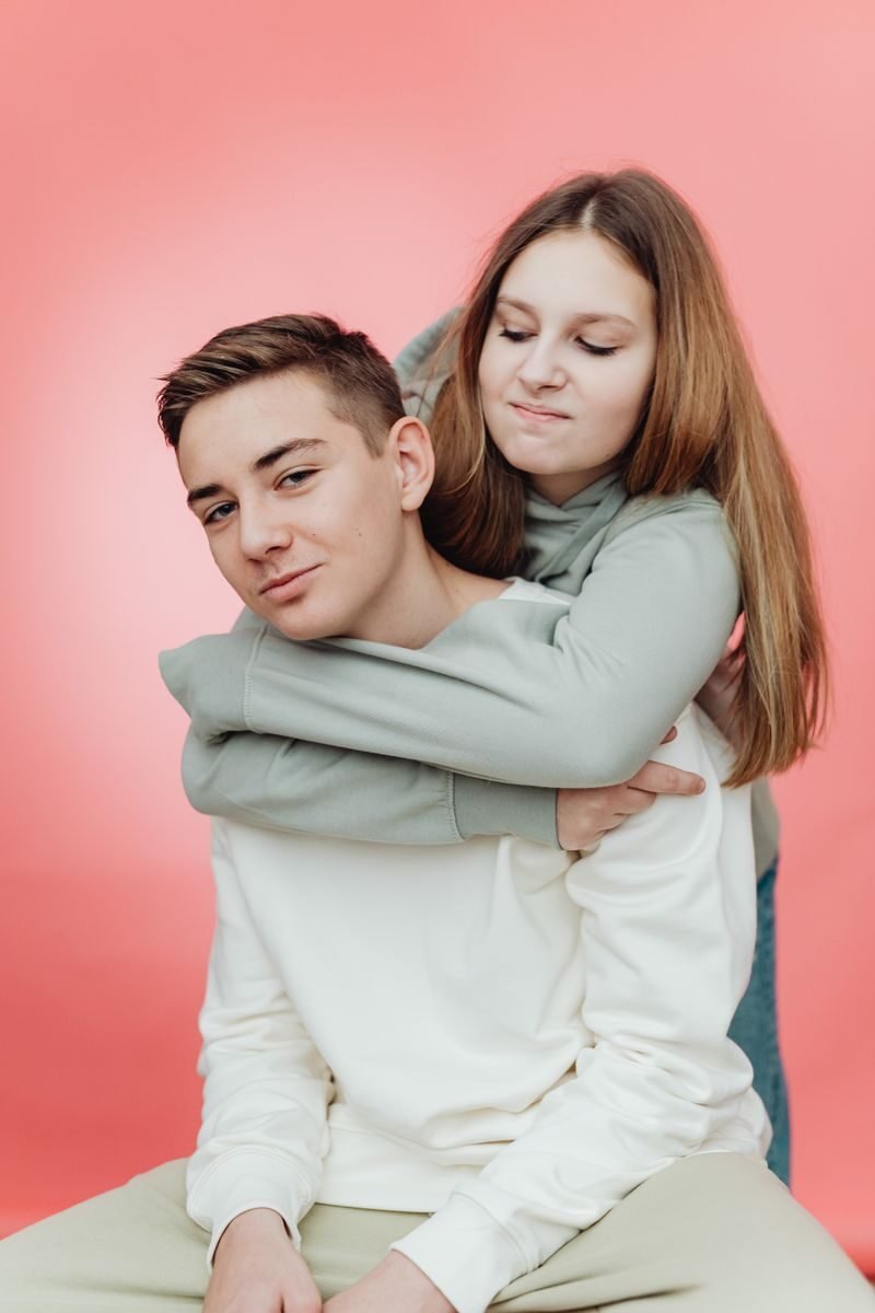 A relaxed portrait of a young couple in casual attire with a warm expression on a pink background.