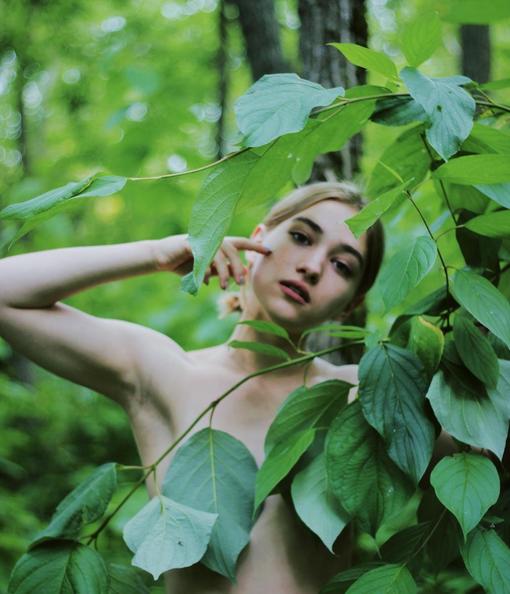 A creative portrait of a woman posing gracefully in a natural setting, surrounded by vibrant green foliage.