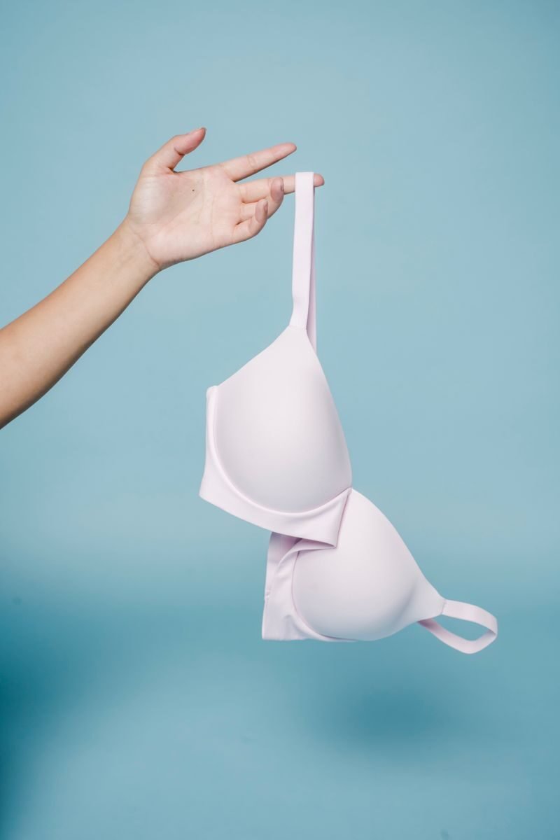 Crop anonymous female reaching out hand and demonstrating white bra against blue background in studio
