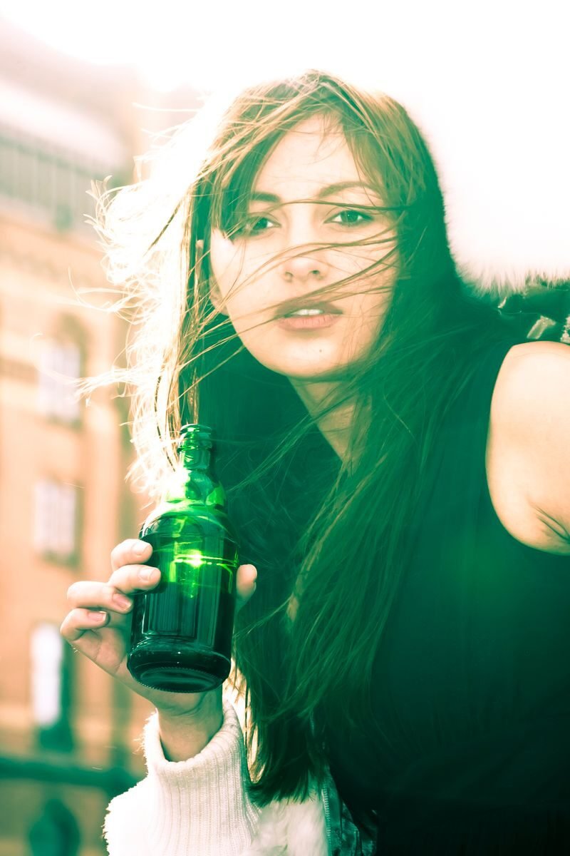 Fashionable woman with long hair holding a beer bottle in Hamburg, Germany, outdoors.