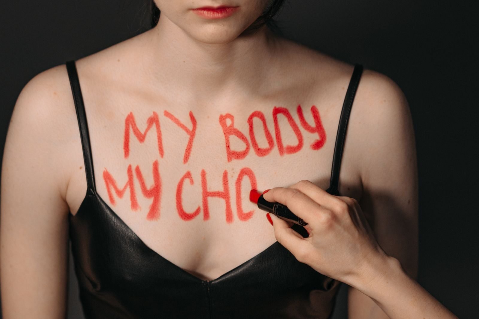 Close-up of a woman with 'My Body My Choice' written on chest in red lipstick.
