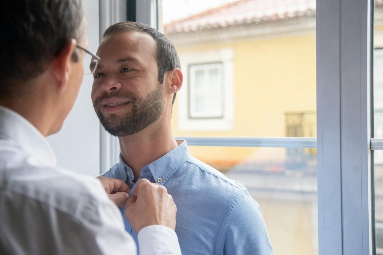 Two men in a loving moment by a window in Portugal, expressing affection and togetherness.