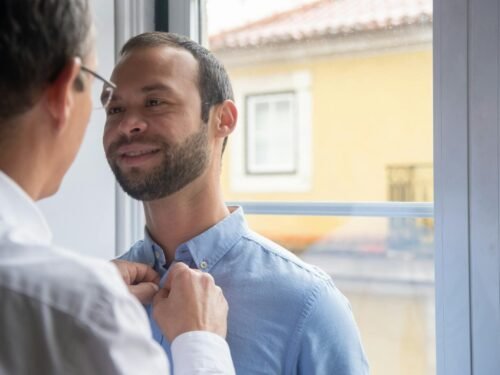 Two men in a loving moment by a window in Portugal, expressing affection and togetherness.