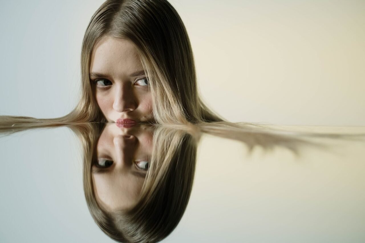 A woman's face reflected in a water-like surface, creating a mirrored effect.