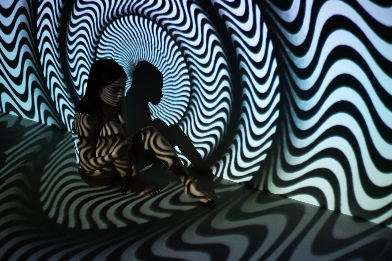 A mysterious and surreal scene featuring a woman sitting in a wavy optical illusion pattern.