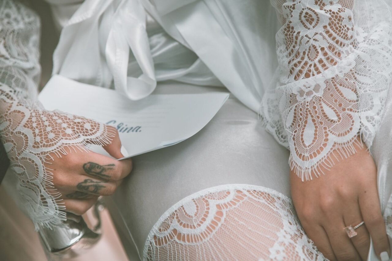 Side view of crop unrecognizable tattooed bride in elegant lace dress holding letter with vow before wedding ceremony