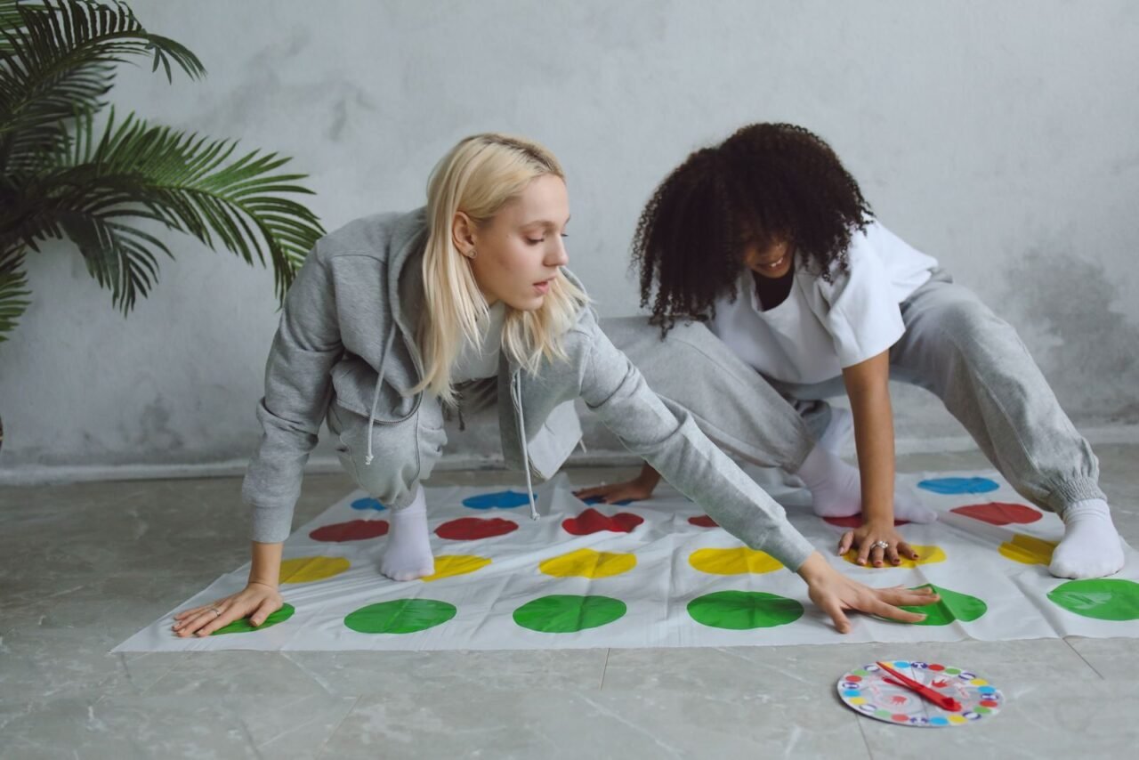 Two young women enjoying a game of Twister in a cozy indoor setting, having fun and relaxing.