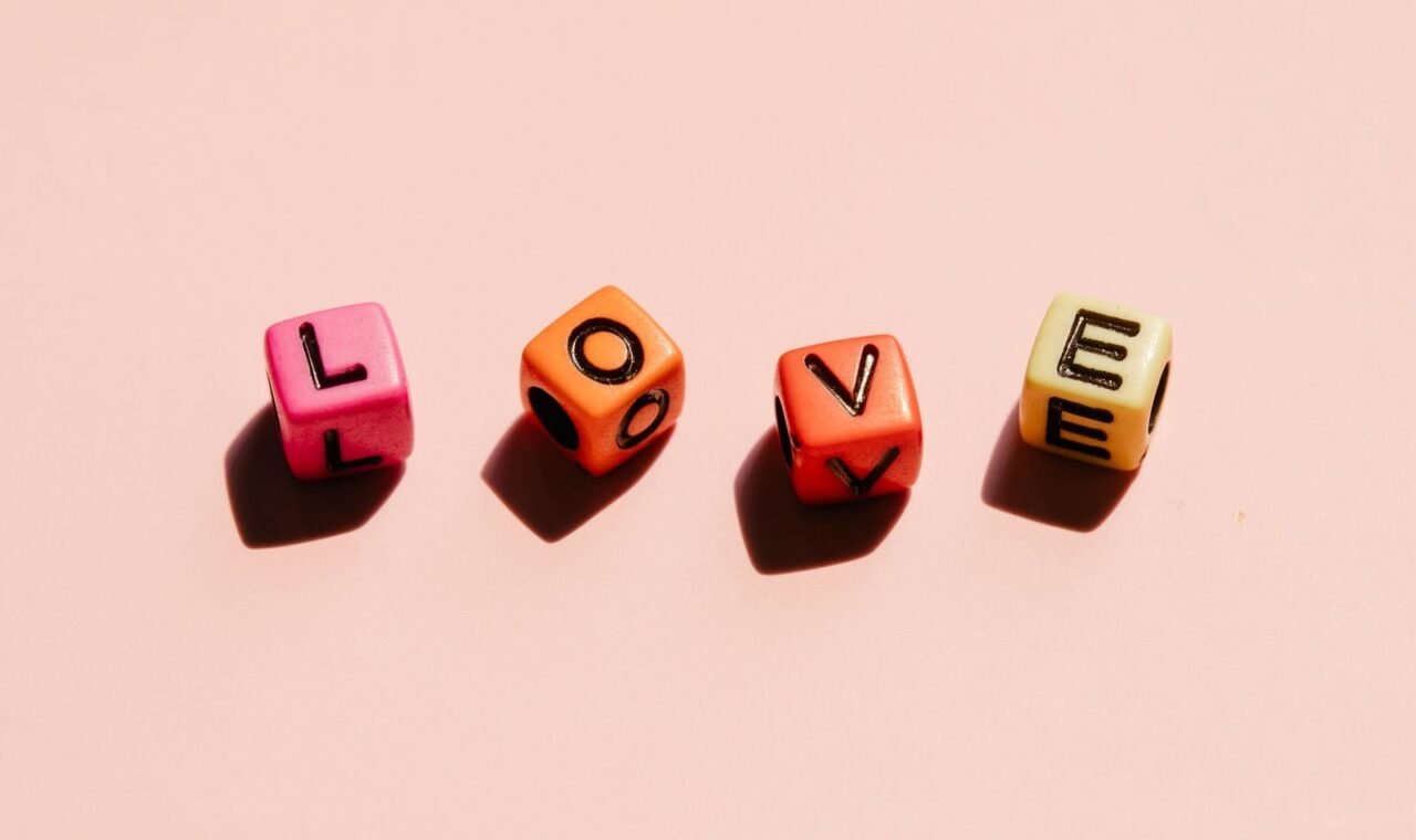 Close-up of colorful dice spelling 'LOVE' on a pastel pink background, symbolizing affection.
