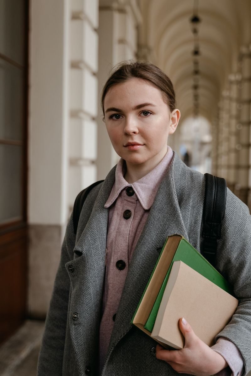 Young woman standing in a corridor holding books, conveying a scholarly vibe.
