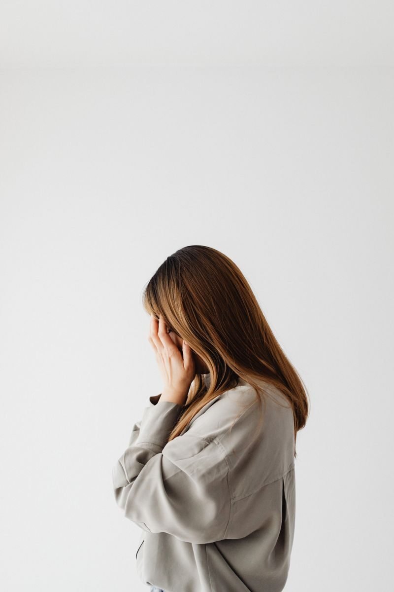 Side profile of a young woman with brown hair covering her face, creating a thoughtful expression.