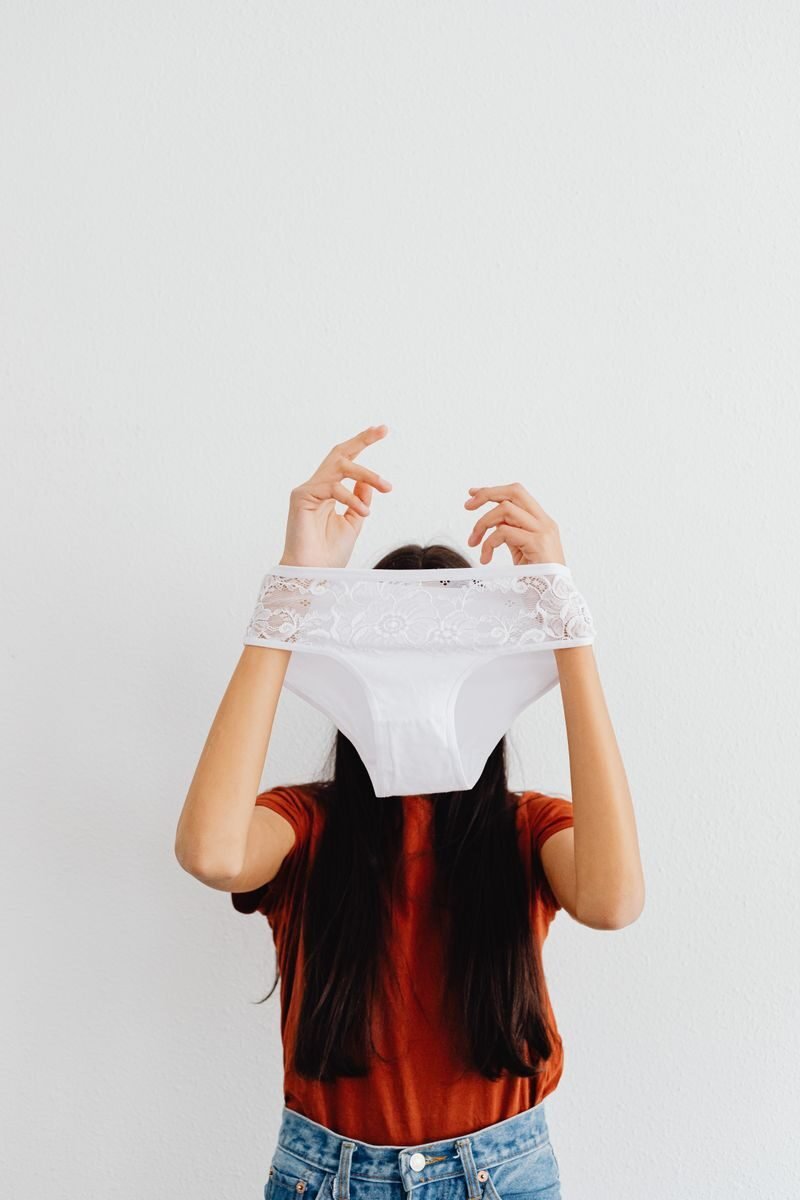 A woman playfully holding a white lace panty against a minimalist white background.