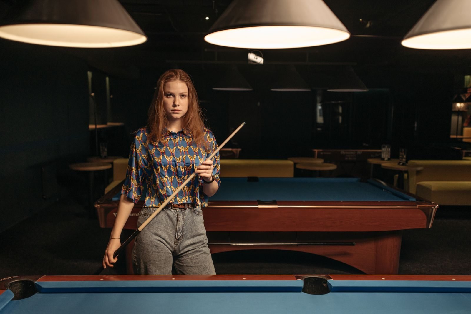 Woman with a cue stick standing in a billiard room preparing to play pool indoors.