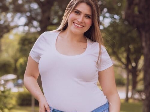 A cheerful woman standing in a park, wearing a white shirt and jeans.