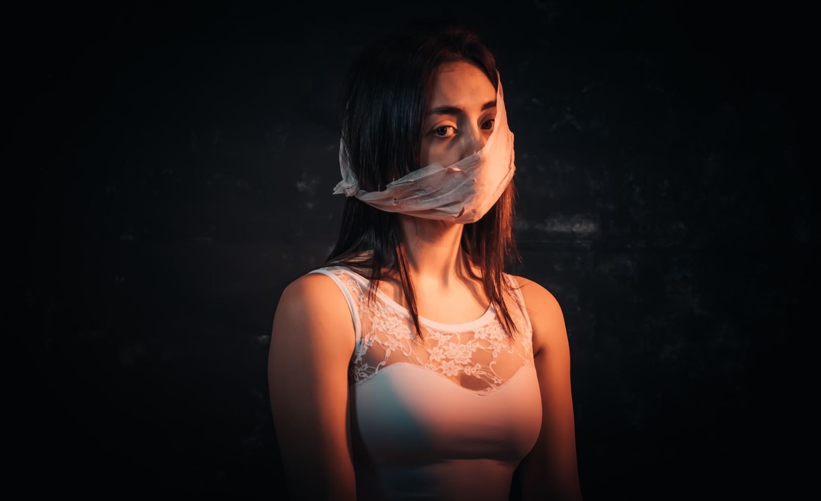 Dramatic image of a woman in a lace dress with gagged mouth, expressing deep emotion and introspection.