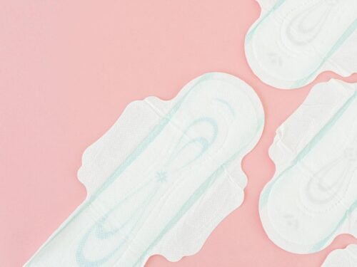 Top view of sanitary pads arranged on a light pink background with ample copy space.