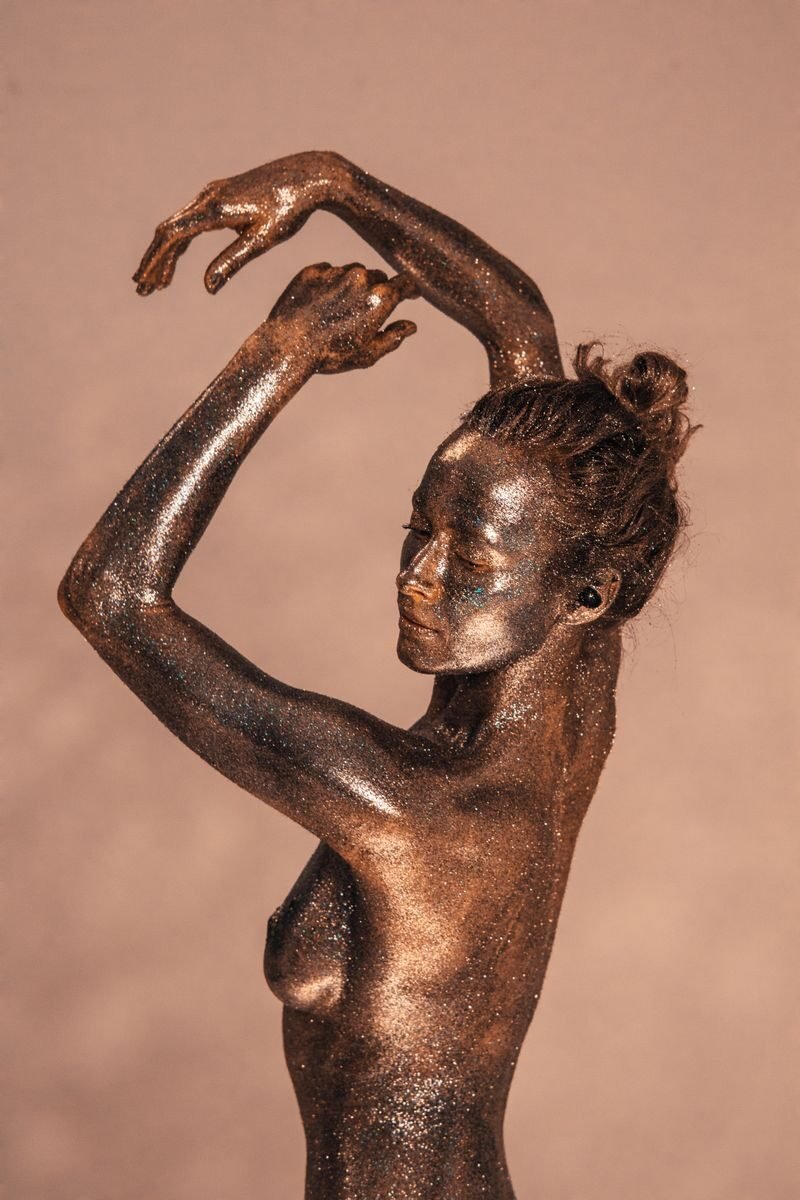 Elegant pose of a woman covered in bronze body paint and glitter.