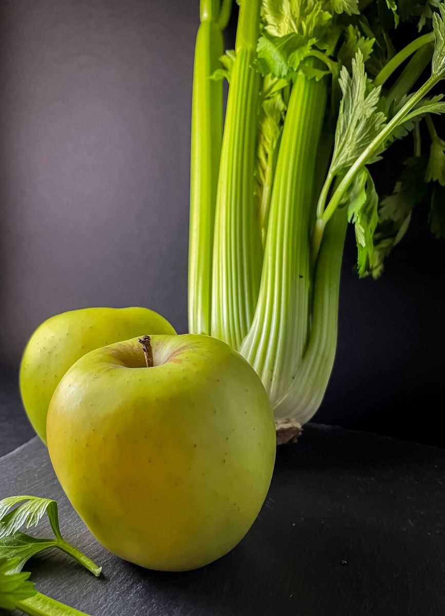 A still life of fresh green apples and celery stalks on a dark surface, emphasizing healthy food.