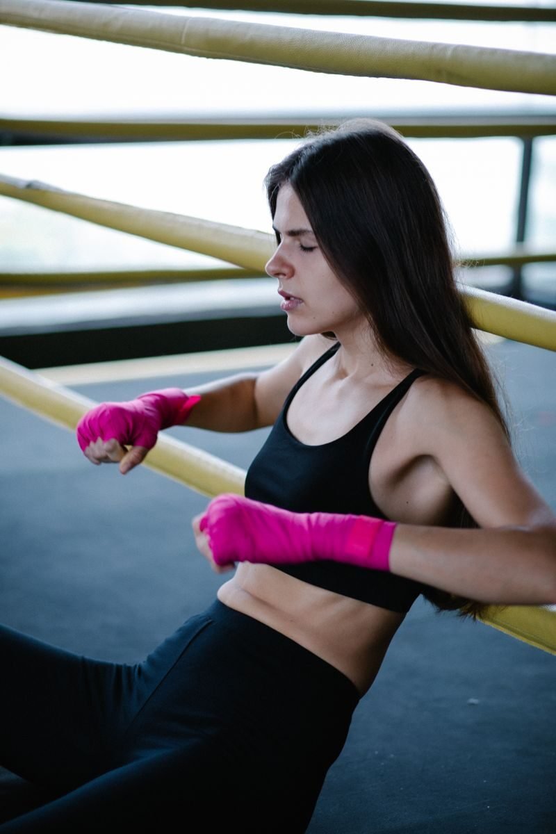 A female kickboxer sits exhausted in a boxing ring, wearing pink gloves.