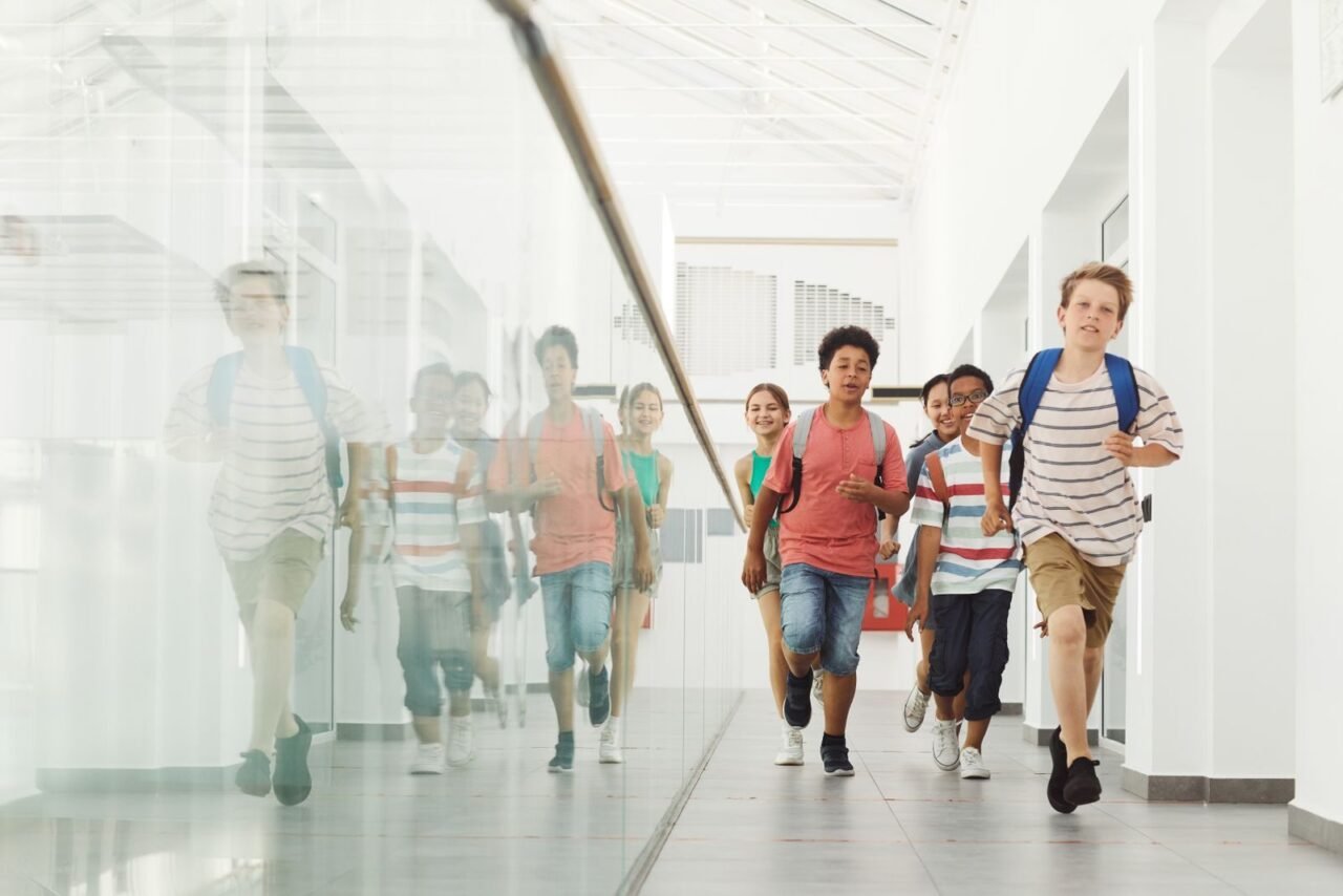 Group of diverse kids joyfully running in a bright school hallway.