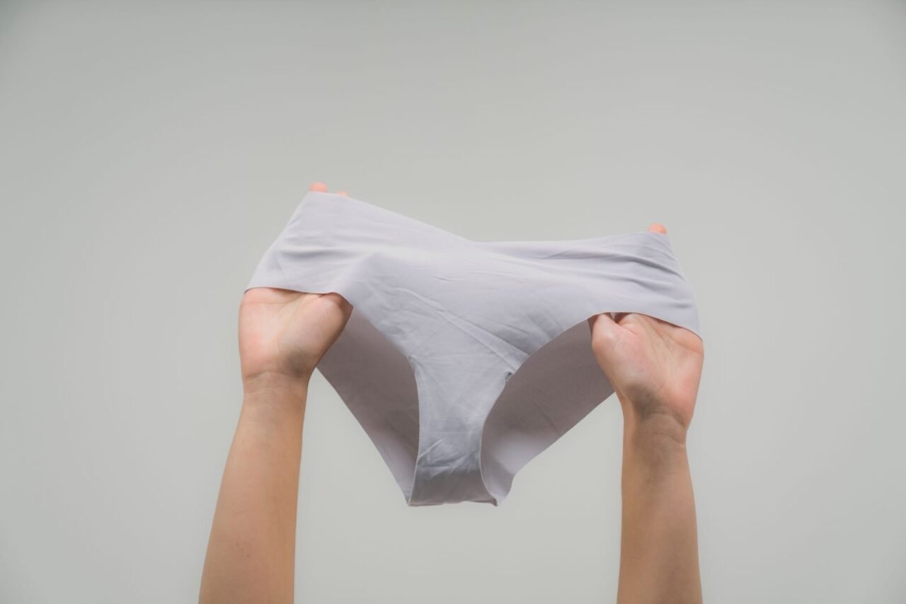 Hands holding a white undergarment against a plain backdrop, symbolizing women empowerment.