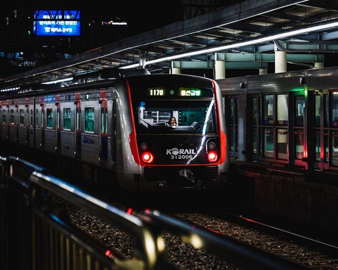 A Korail train at night in a bustling Seoul station, illuminated with vibrant lights.